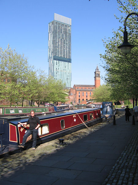 Woman stood by moored narrowboat with Hilton Hotel Manchester in background